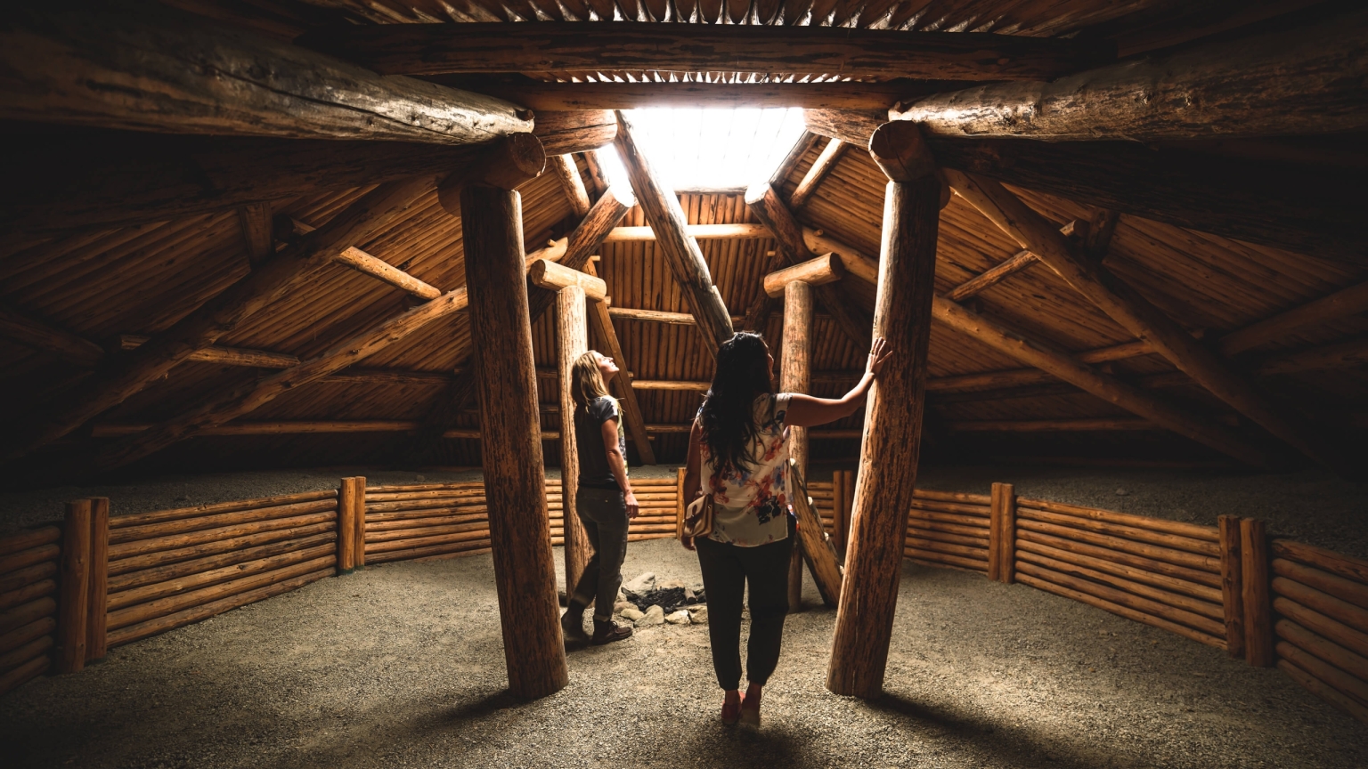 Two women look up through an opening in the ceiling at the Nk'Mip Desert Cultural Centre