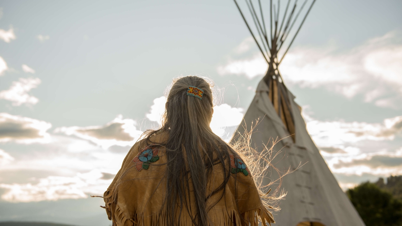 Ktunaxa elder in regalia next to a teepee at St Eugene Golf Resort