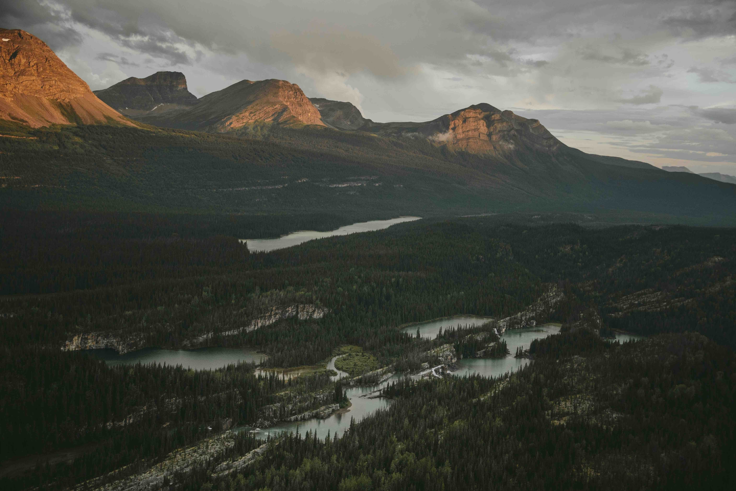 A mountain range at sunset in the Northern Rockies. A river system flows in the valley below.