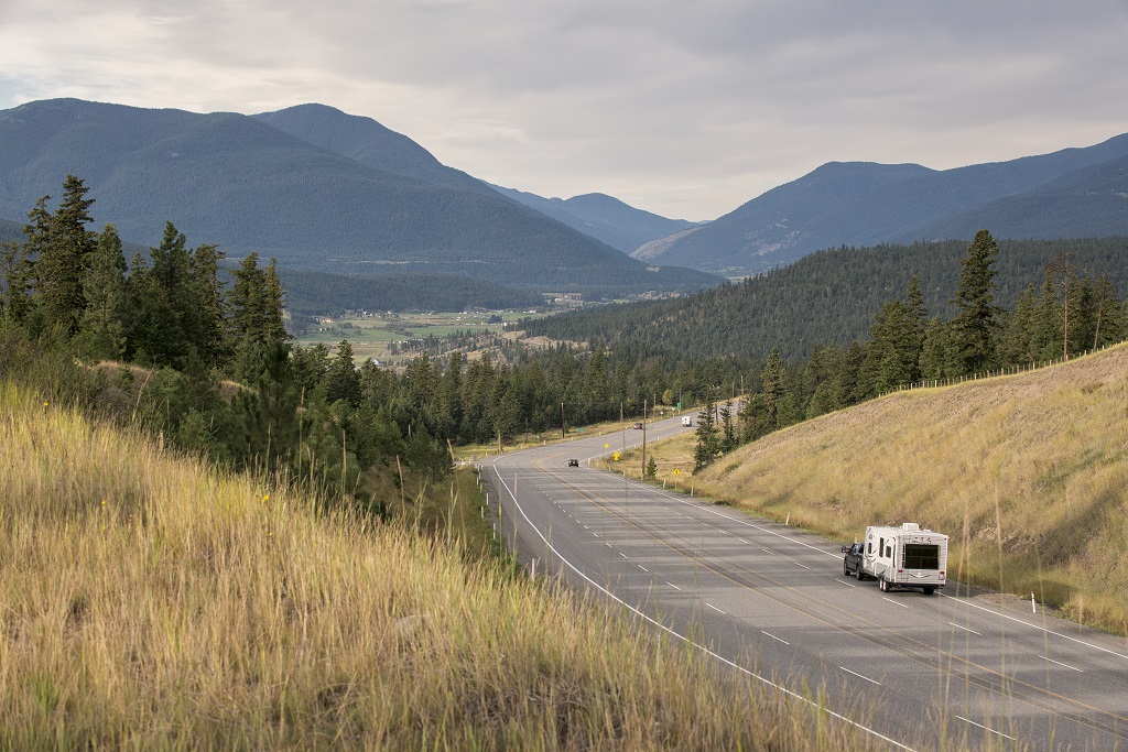 An RV travels down a highway, towards a mountainous landscape.