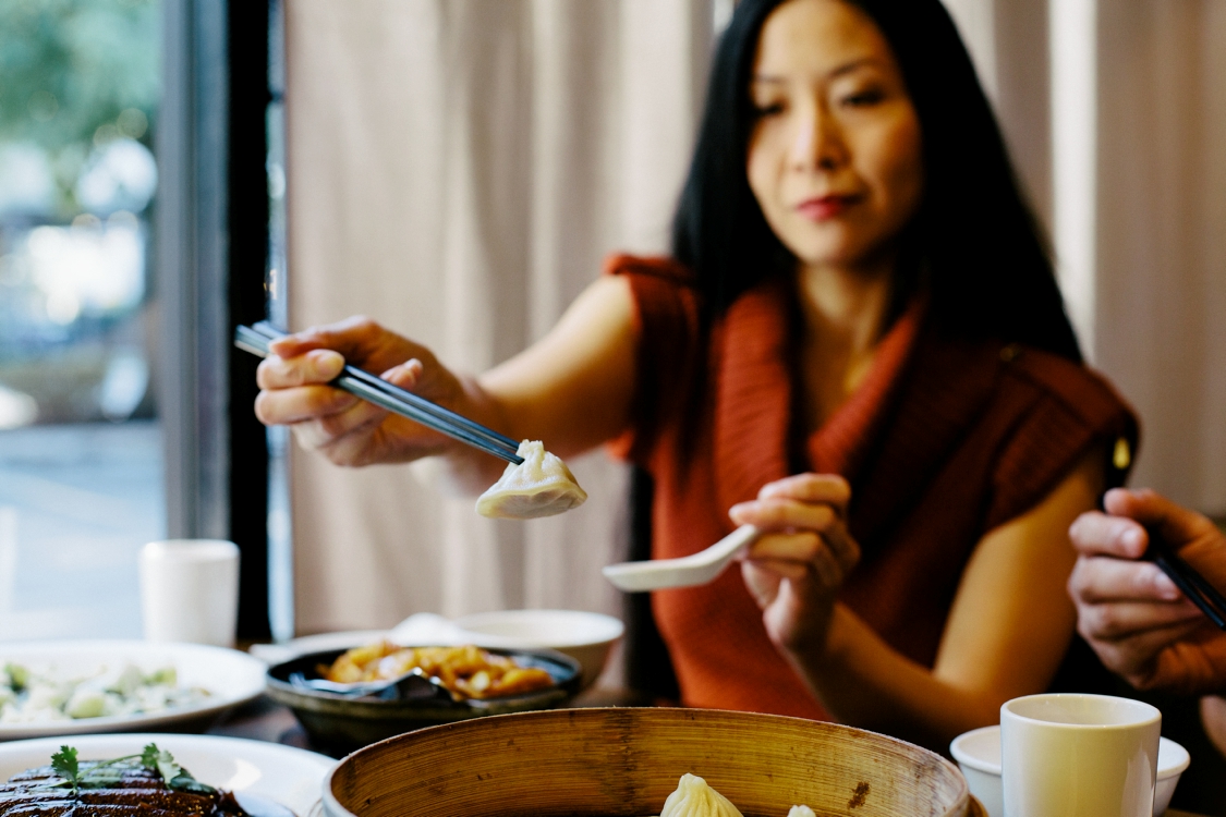 A woman lifts a dumpling out of a basket at a restuarant in the 