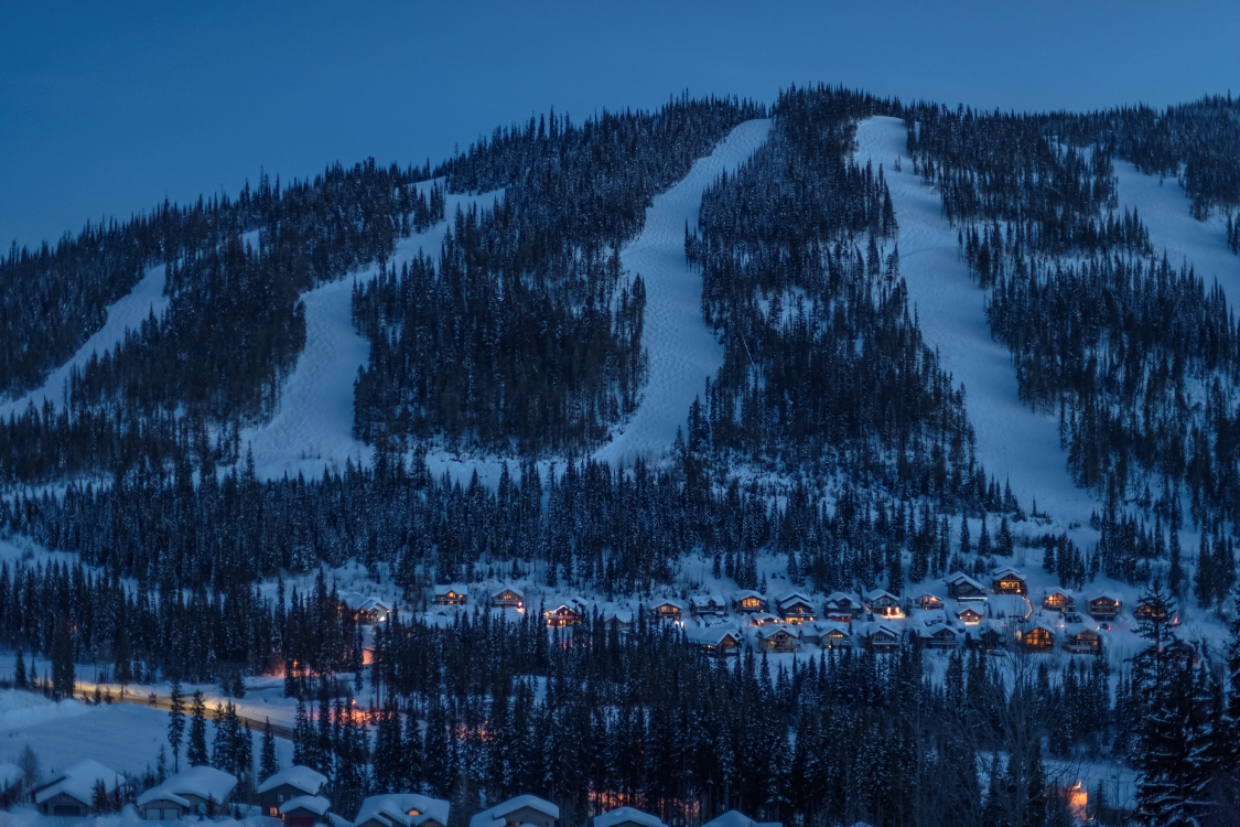 Sun Peaks Resort at dusk with twinkling village lights at the mountain base.
