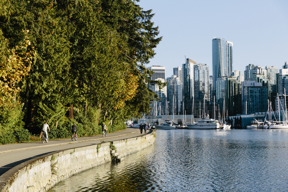 People walk along the seawall in Stanley Park in the summer time. Downtown Vancouver is seen in the background across the water.