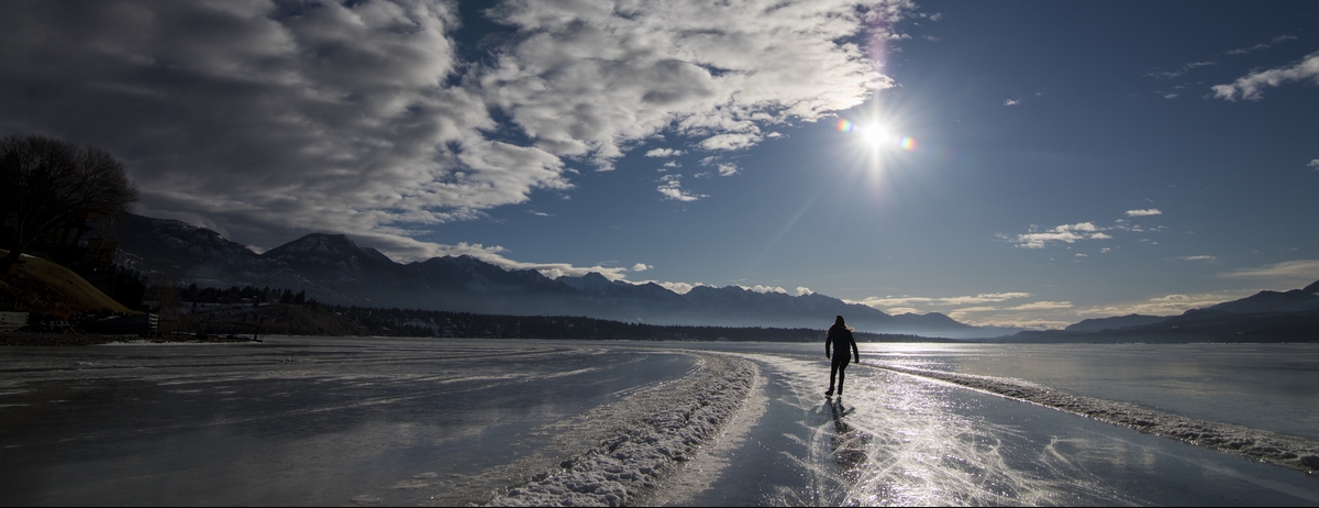 A person skates off in the distance under blue skies on the Lake Windermere Whiteway