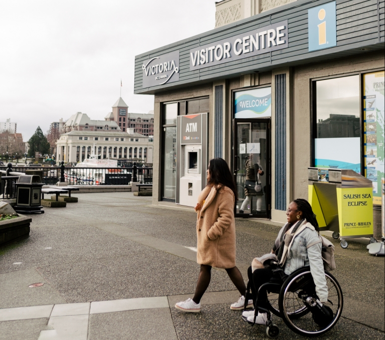 Two people depart the visitor centre in Victoria and move through the parking lot.