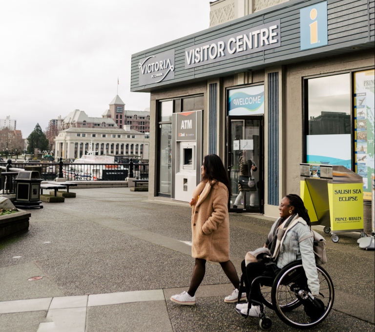 Two people depart the visitor centre in Victoria and move through the parking lot.