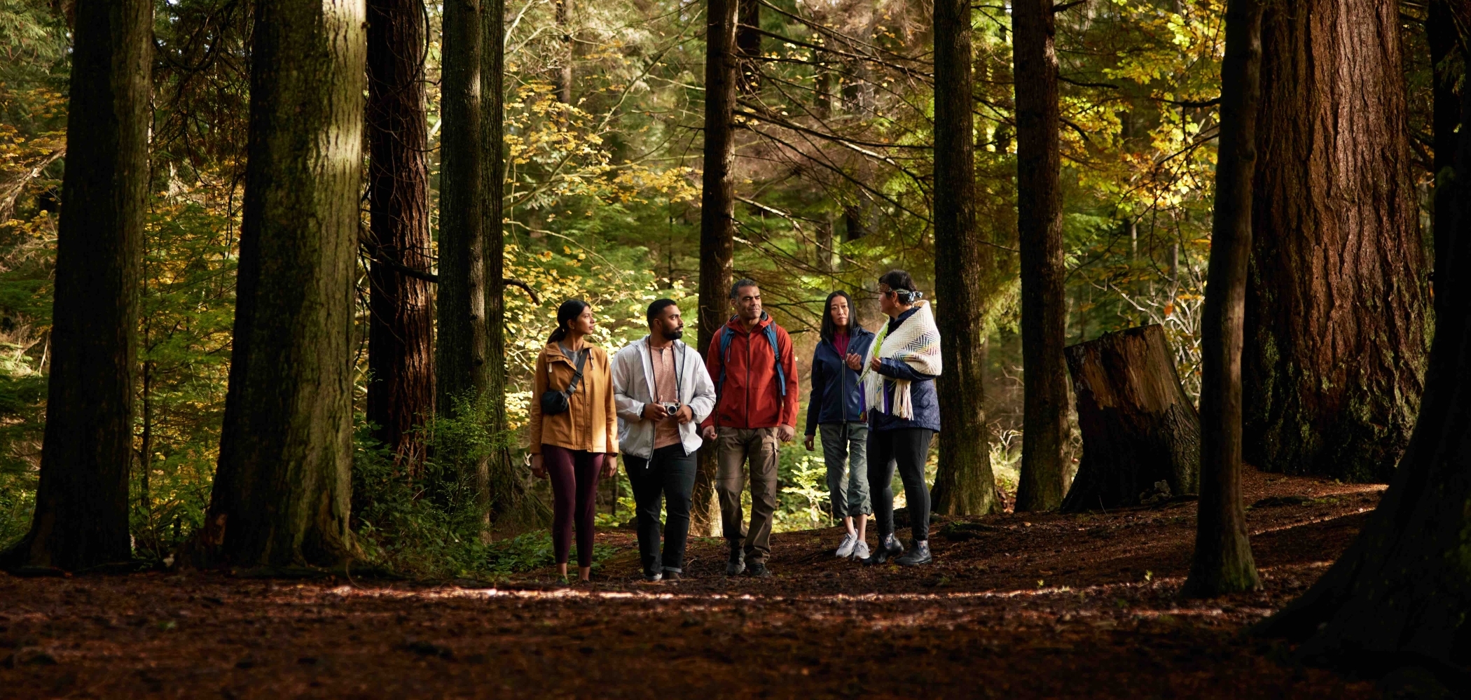 Candace Campo from Talaysay Walking Indigenous Tours is conducting a presentation and speaking to a group while on a walking experience in Stanley Park in Vancouver.