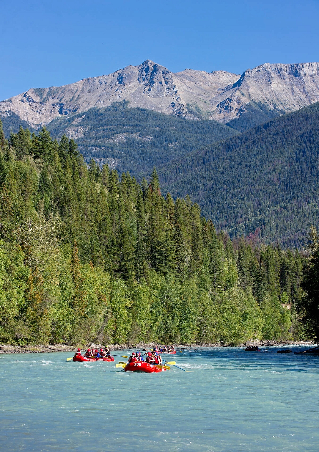 Several boats river raft down a turquoise-coloured river with mountains in the background